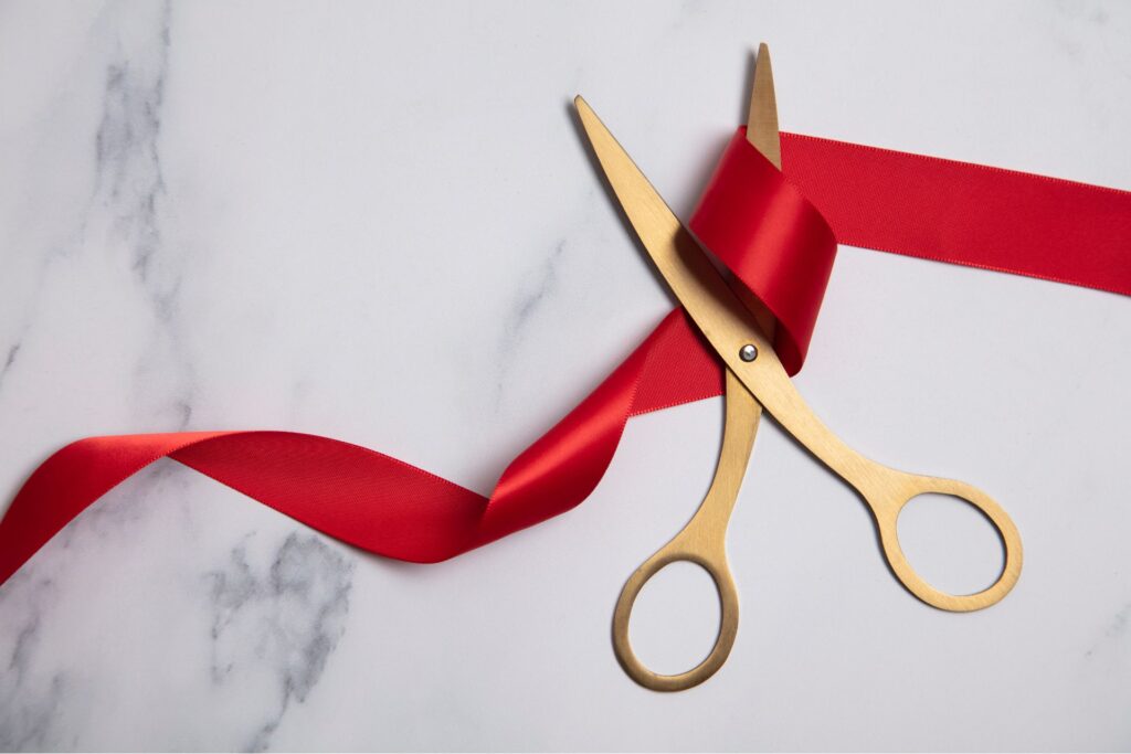 a scissor placed on top of a red ribbon on the marble table symbolizing cutting ties